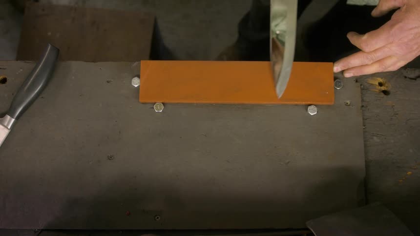 Man stands while honing knife on a block lying on a workbench