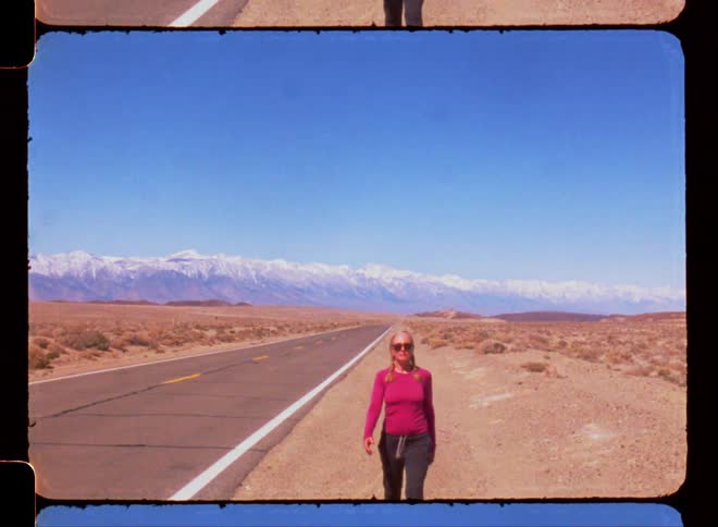 An older white woman walking next to a highway in a desert