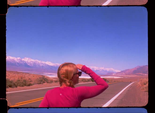 Woman standing next to a road in the desert looking at the horizon
