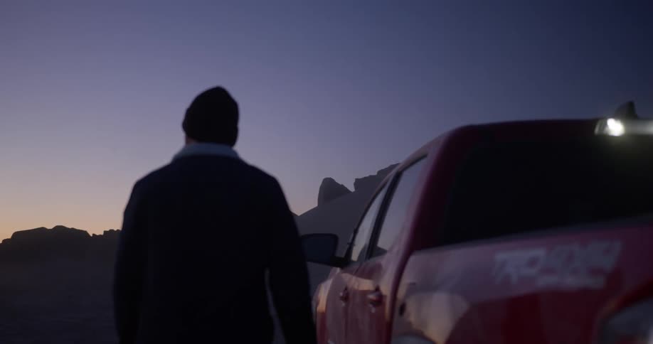 Man getting into his pickup truck in a natural environment with canyons all around on a purple morning
