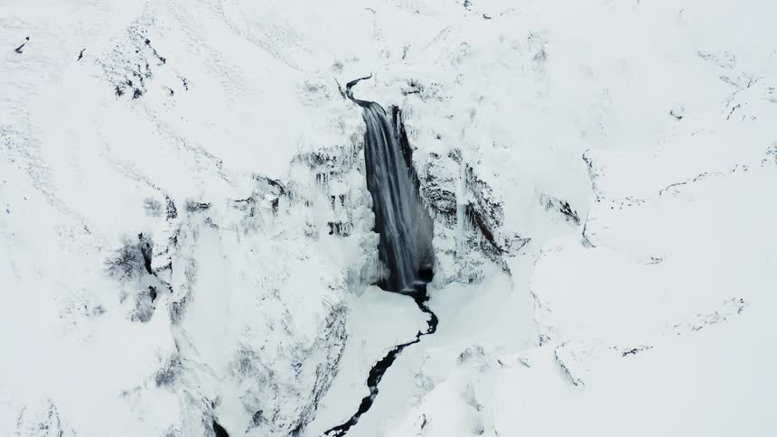 Aerial panorama of snowcapped white mountains and a waterfall with flowing water