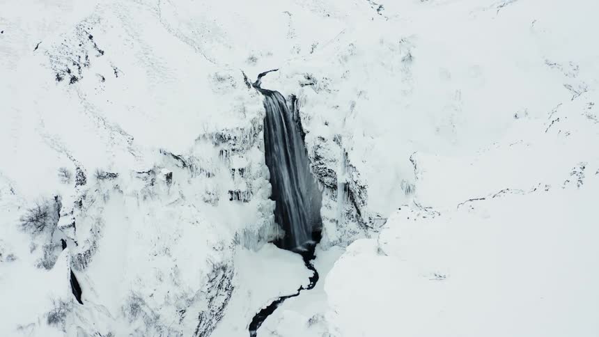 Aerial scene of a waterfall with free falling water in the middle of snowwhite mountains