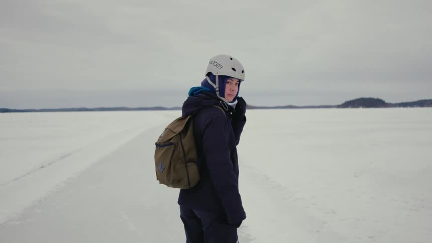 A woman looks to camera as she stands on a frozen lake