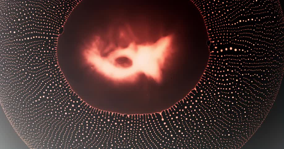 Extreme closeup and a reddish dense drop collapsing and forming a pattern of small abstract drops