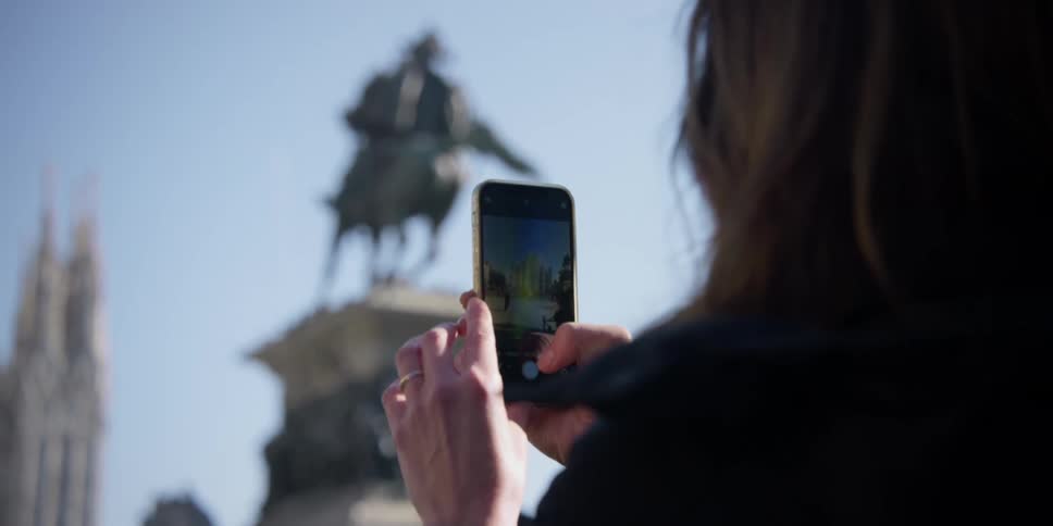 Womans hands holding an iphone and photographing the statue of King Vittorio Emanuele II in Milan