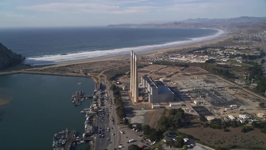 Aerial of a power plant next to an ocean shore on a mostly cloudy day
