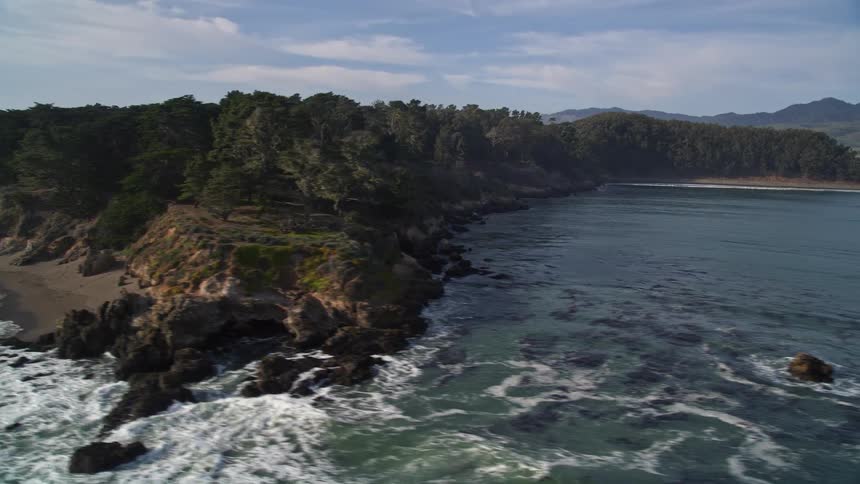 Waves hit rocks on a coast by a bay
