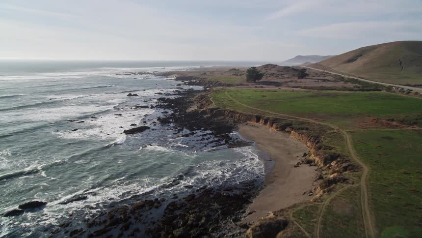 Rocky coastline bathed by the waves of an extensive ocean with a road in the middle of mountainous hills