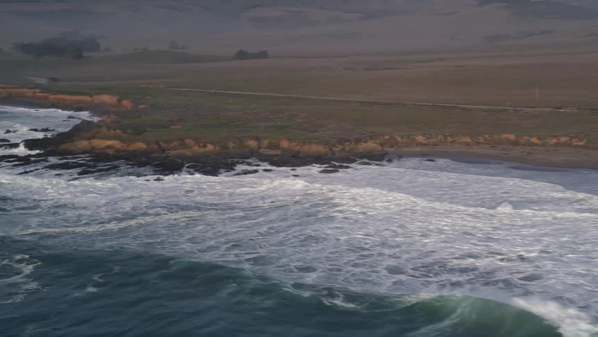 Aerial panorama of blue sea colliding with rocky coast with mountains