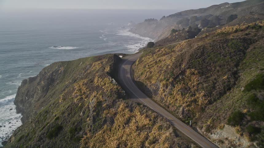 Aerial scene of a long road through the mountains next to an extensive sea