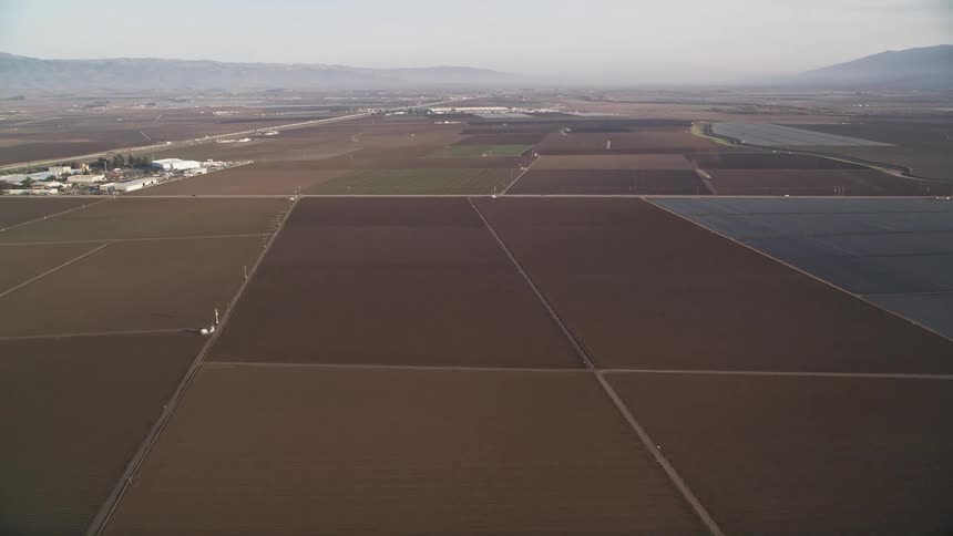 Aerial view of agricultural fields divided into rectangular plots with silhouette of mountains in the background on the horizon