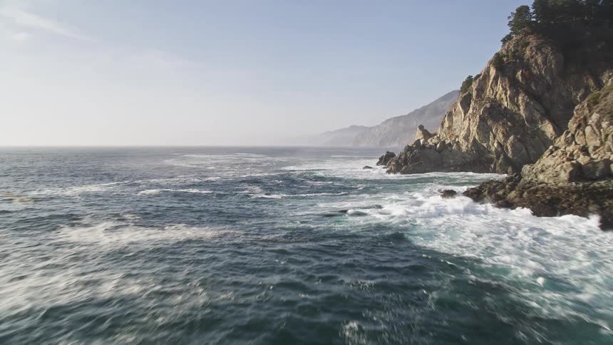 Scenery of a vast ocean with waves crashing on the rocky shore on a clear blue sky day