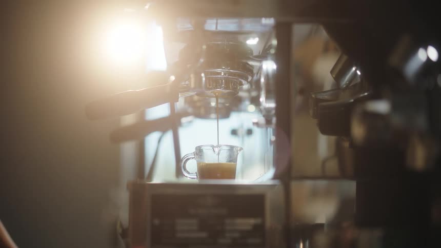 Coffee machine pouring cappuccino into a glass cup with sun glare hitting it in a coffee shop