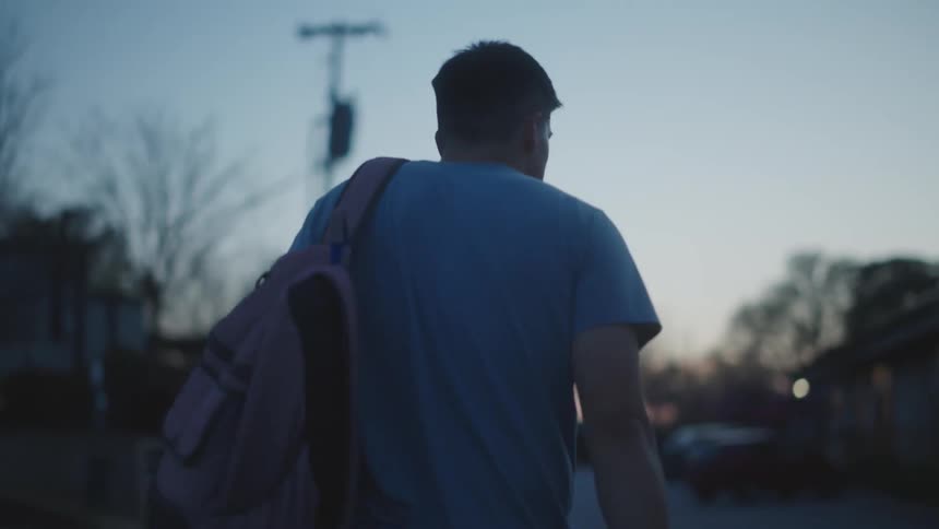 A young man walking down the street at dusk