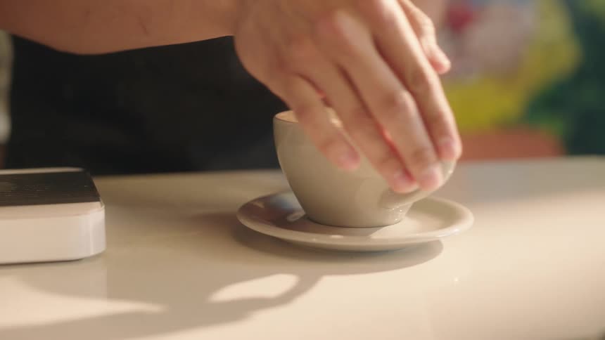 Hands of a man placing a cup with cappuccino on a saucer