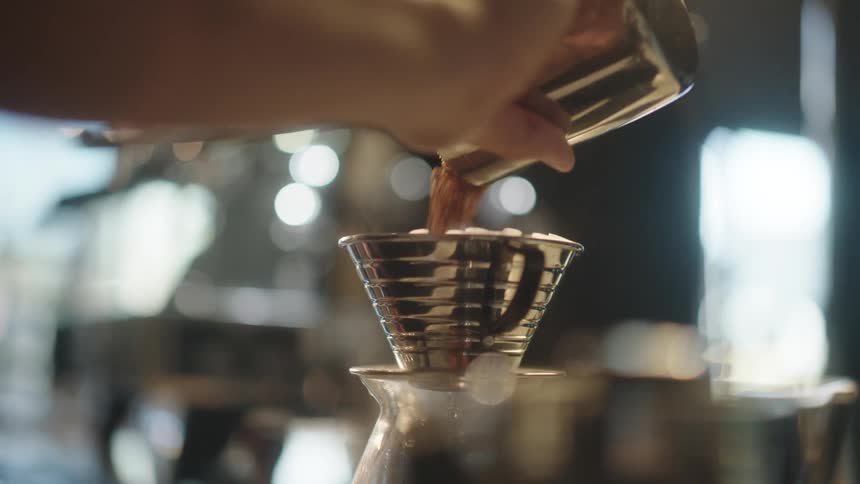 A hand pouring coffee grounds into a metal filter