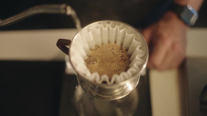 Man preparing coffee and pouring boiling water through a filter into a cup