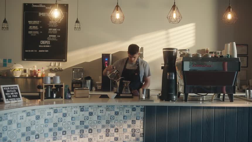 A barista prepares a coffee behind the counter of a coffee shop