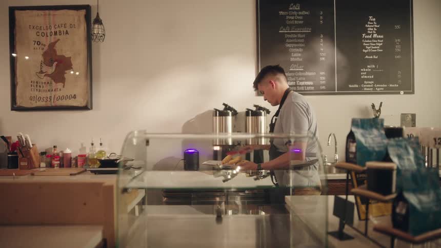 A person is working behind the counter in a coffee shop with a menu board