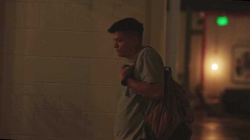 A young man with a backpack exits a building