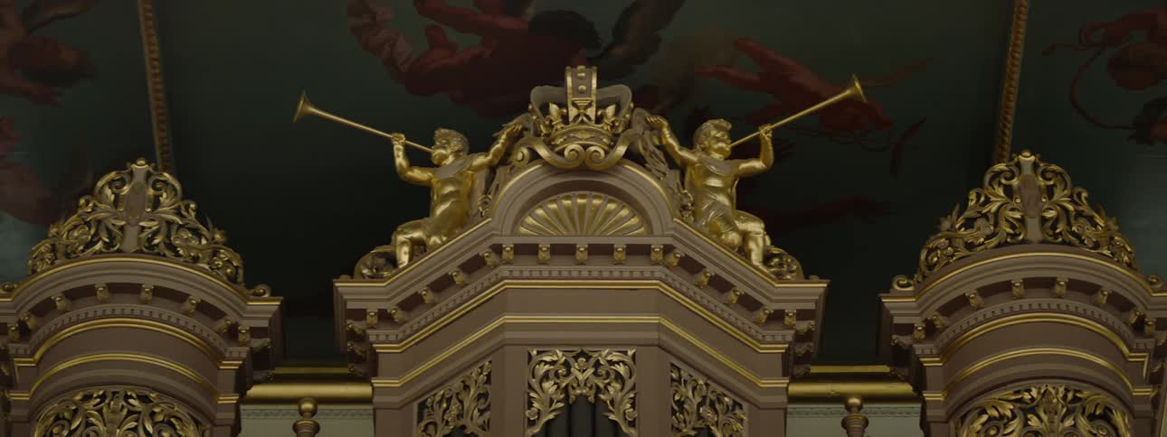 Golden statues and elaborate decorations top columns under painted ceilings in large room
