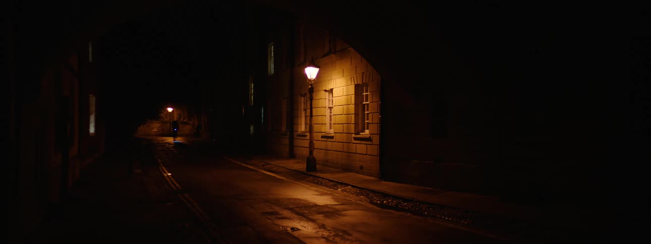 Dark street at night in an old city with vintage lampposts and the silhouette of a person passing by on a bicycle