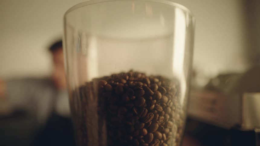 A man pours coffee beans into the glass