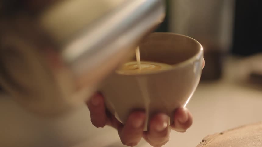 Closeup of a persons hand holding a cup and pouring milk into coffee