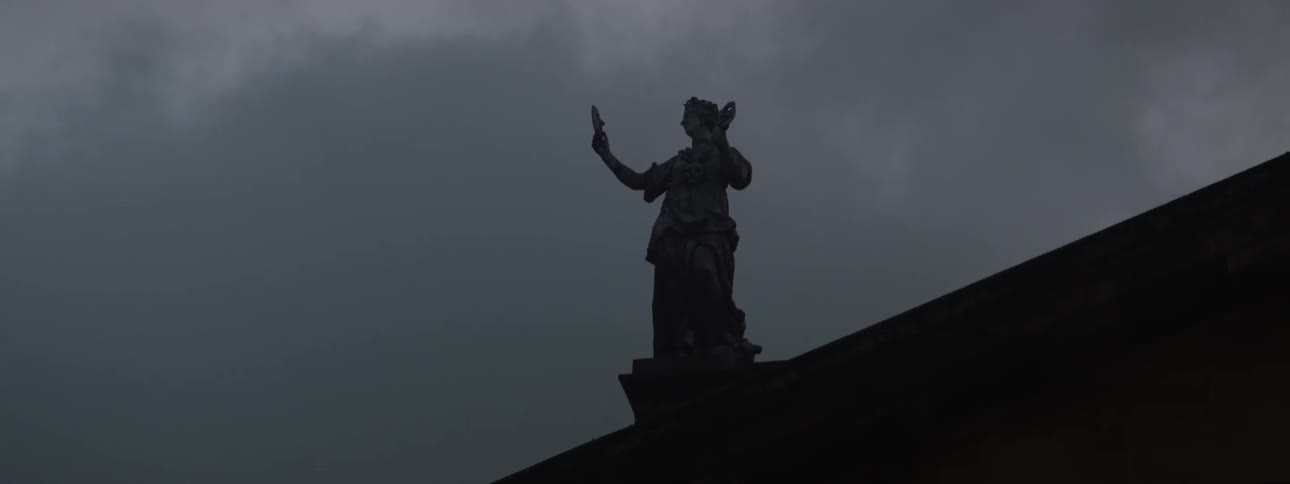 Silhouette of a statue on the roof of a building under an overcast sky