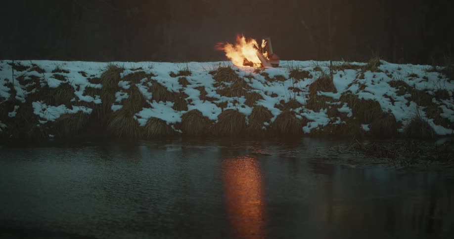 A fire burns on a river bank