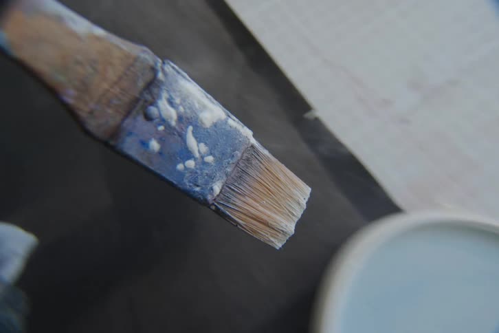 POV closeup of a paint brush with a wooden handle and frayed bristles painting