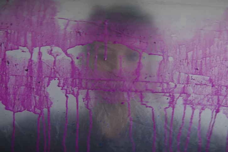 Womans face in a foggy window with pink paint running down
