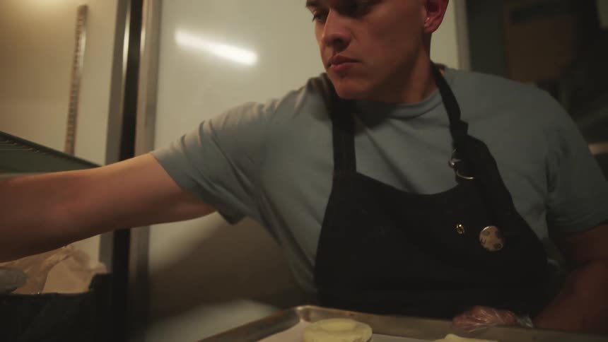 A restaurant employee arranges bagels on a baking pan
