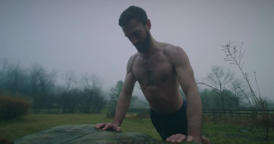 Man doing pushups shirtless on a rock outdoors on a cloudy day