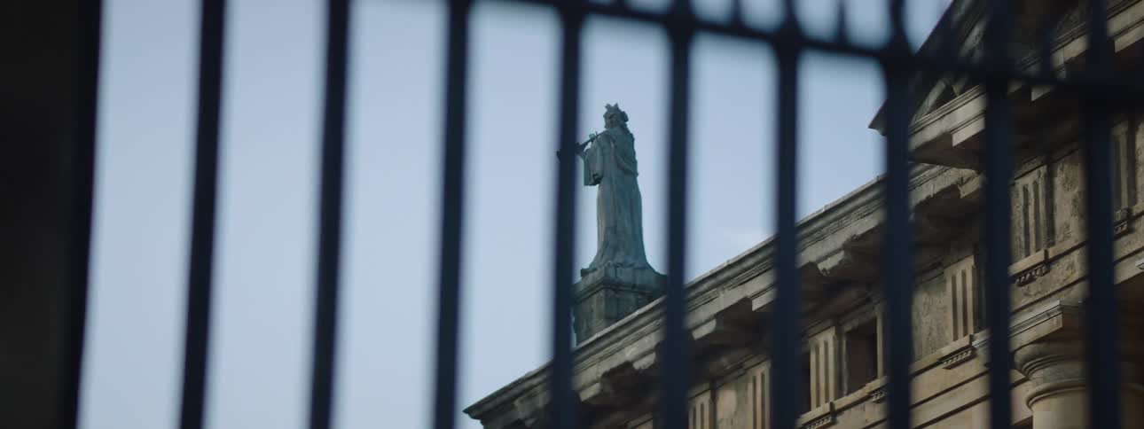 A statue on a manorial estate home seen through a metal fence