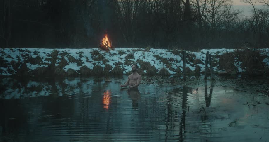 A man stands in deep water as a fire burns behind him