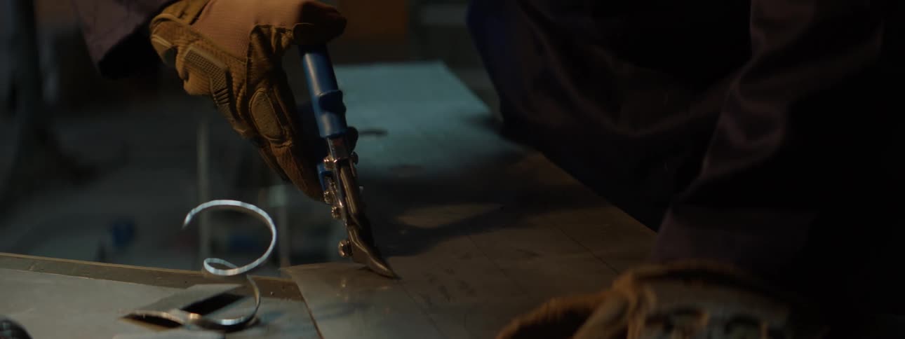 Hands of a person wearing gloves and holding a pair of pressing and cutting pliers on a metal rod