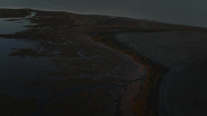 Entry to harbor sits across water from town on nearby land under a red tinted horizon