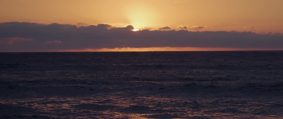 Footage of the ocean at sunrise with the sun peeking just above the clouds