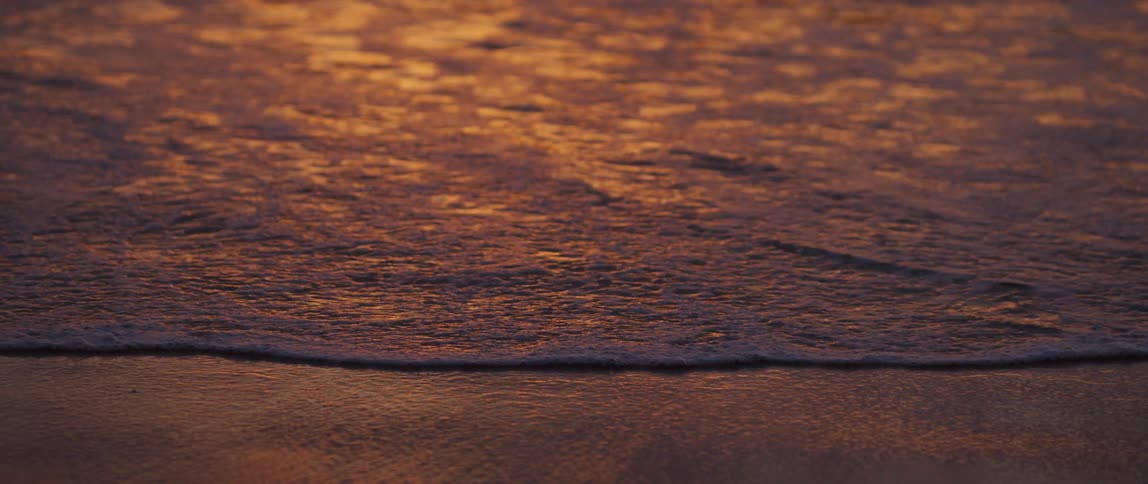 Ocean waves slowly rolling in to a beach at dawn