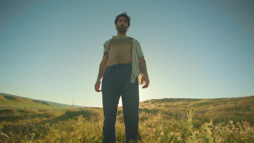 Man in an open shirt with his chest showing in a natural field in daylight