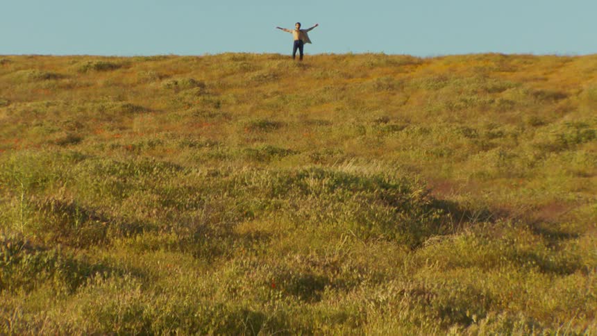 An almost shirtless man dances in a field