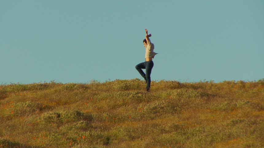 A white man dances on a grassy plain