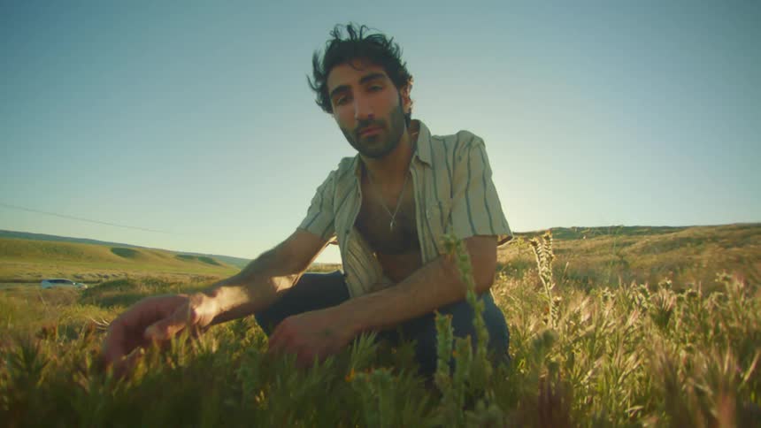 A man squats in a grassy field