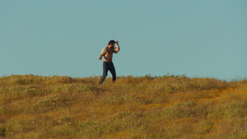Man on a hill dancing on a cloudless blue sky day
