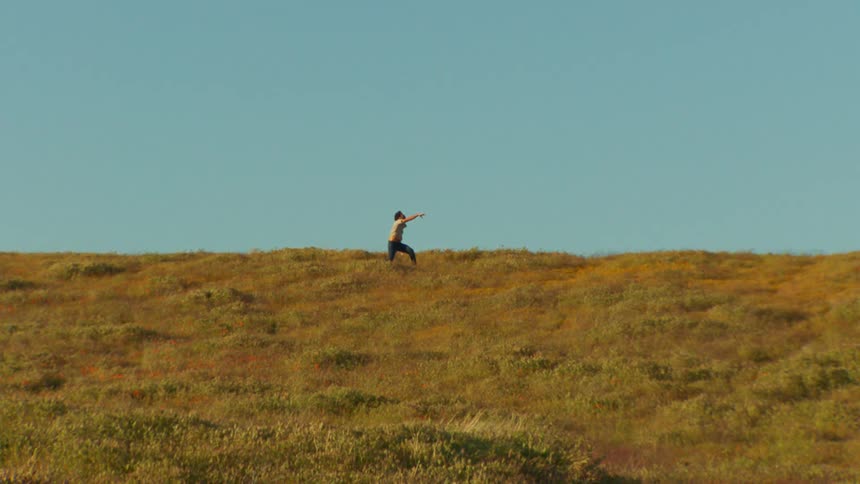 Man on a hill dancing on a cloudless blue sky day