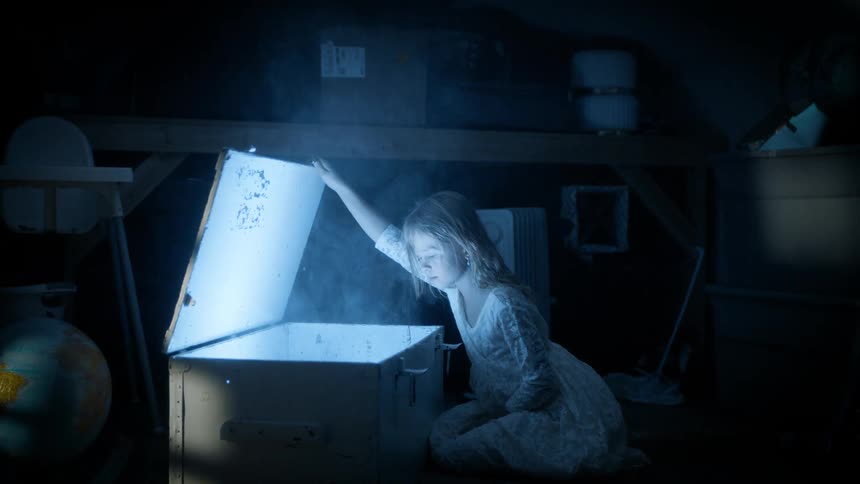Girl inside a dark room looking at an open box with smoke and a light emerging