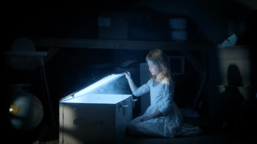 Girl in a dark room opening a box and a bright light begins to emerge