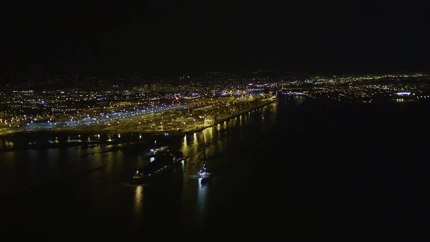 An aerial view of a city in front of a sea and it is night and the city is all lit up
