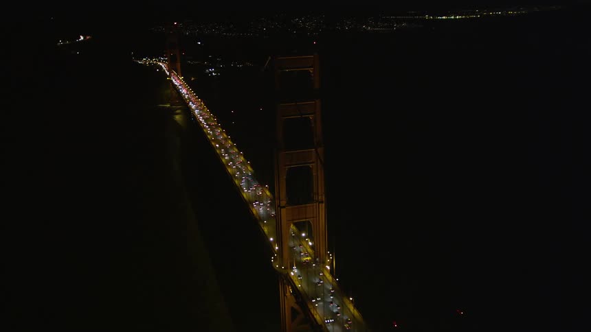 Aerial panorama of a long bridge over the sea illuminated at night with vehicle traffic